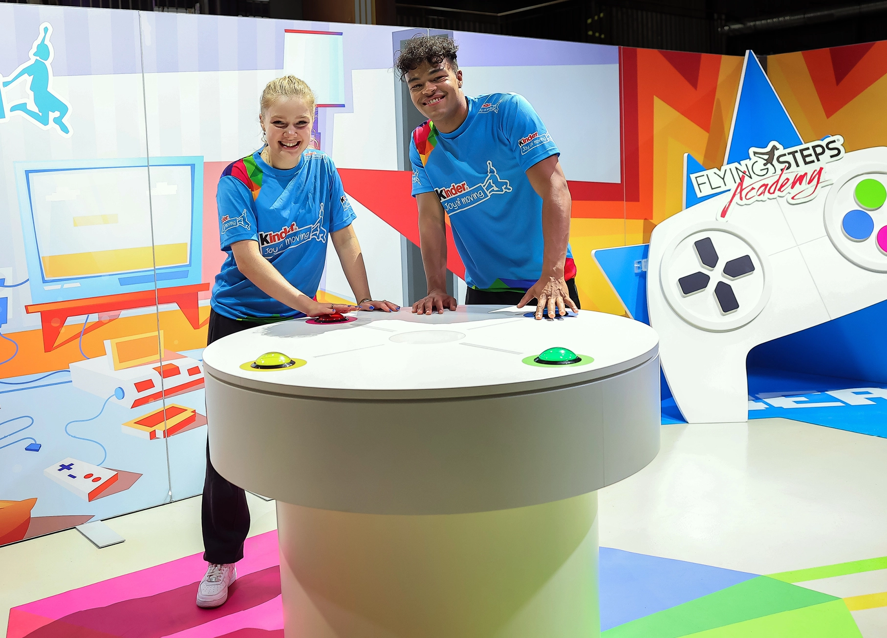 Zwei Markenbotschafter / Influencer lehnen auf einem Spieltisch. Große Arcade-Buttons sind in die Oberfläche integriert um das Rhytmusgefühl der Kinder zu testen. Im Hintergrund ist eine große Event-Kulisse eines Controllers und die Illustration eines Kinderzimmers zu sehen.