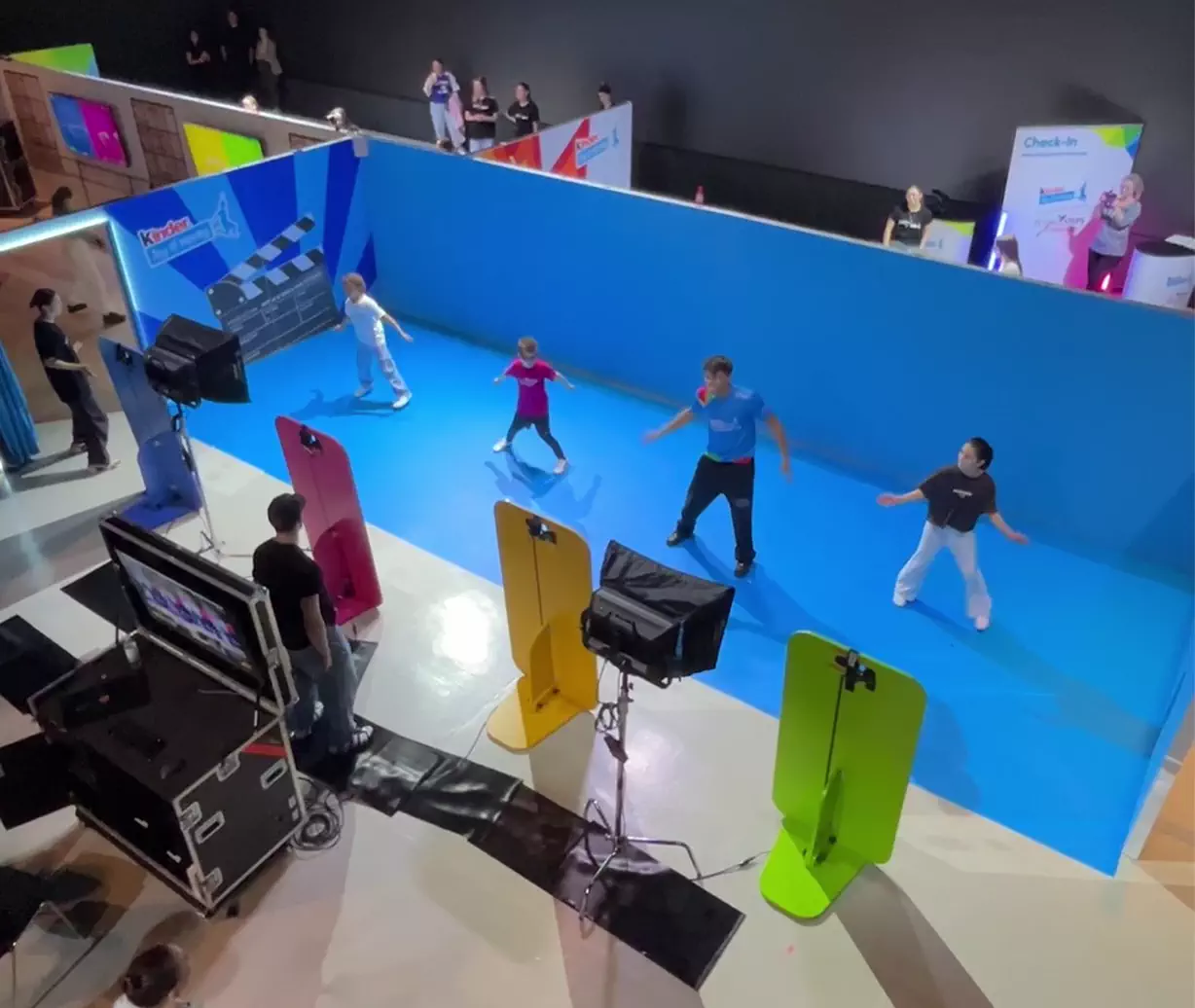 Eine Videoaufnahme von oben: Die Kinder tanzen mit einem Influencer zusammen in einem Green Screen Bereich.