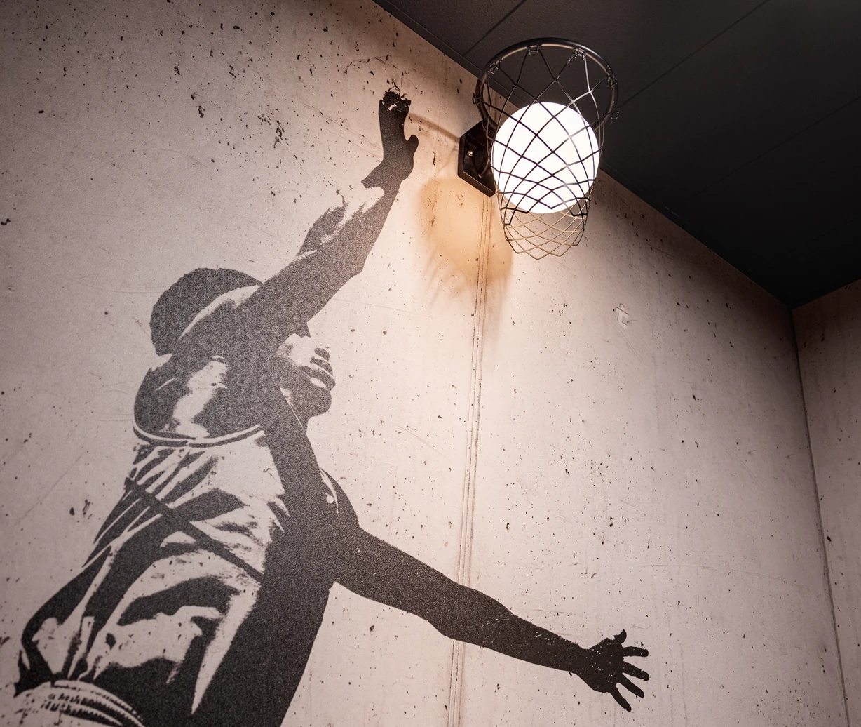 Office-Konzept: Die Grafiken im Flur zahlen auf die Marke ein. Sie zeigen einen Sportler und verbinden sich mit dem Lichtkonzept – eine Leuchte in Form eines Basketballkorbs.