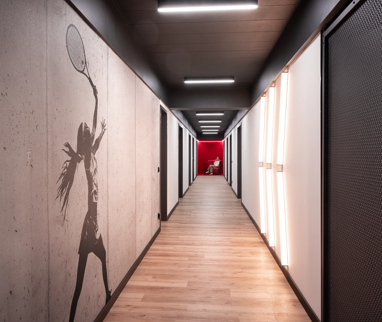 Office-Konzept: Umgestalteter Flur mit grafischer Wandgestaltung und Lichtkonzept. Ein Telefonplatz am Ende des Flurs in der Markenfarbe als Eyecatcher.