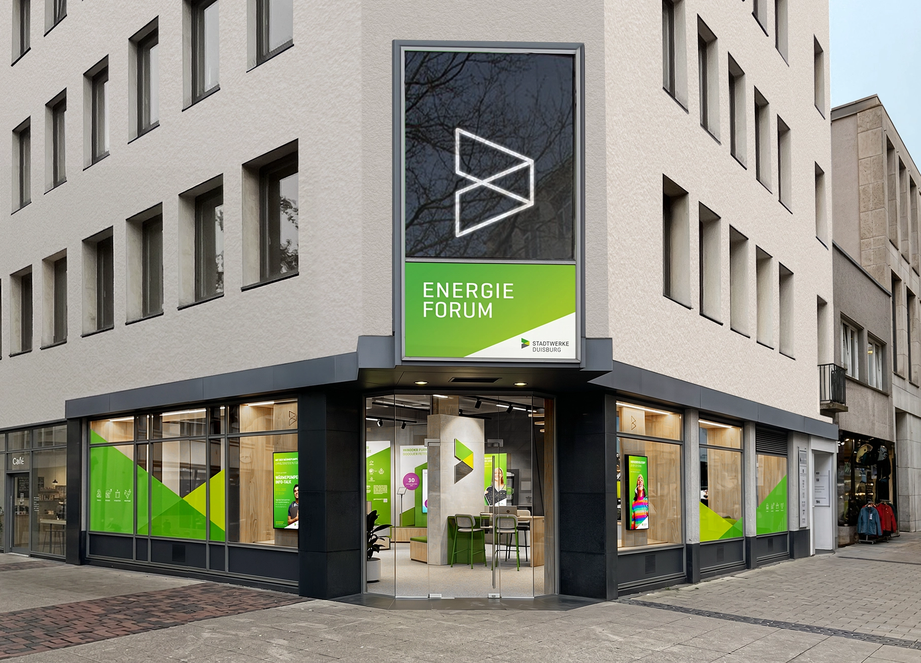 Ehemaliger Retail-Store in Innenstadtlage wird zur multifunktionalen Ausstellungs- und Bürofläche. Der Eckshop mit großer Glastür zeigt die Inneneinrichtung mit Blick auf ein großes Leuchtlogo. In den Schaufenstern sind Holzstelen mit Instore TV Lösung. Die scheiben sind im Stil der Marke foliert. Im Fenster im ersten OG ist ein großes Neon-Logo des Marken Signets.